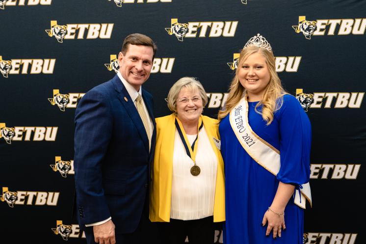 Two women and a man smiling at the camera in front of a navy blue ETBU backdrop