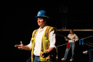 The man is in the foreground with a yellow vest in Working: The Musical Theatre production.