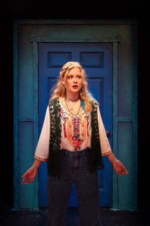 woman with arms to side in front of a blue door during Cagebirds Theatre Production