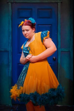 Woman looking at camera with a nervous look in front of a blue door during Cagebirds Theatre Production