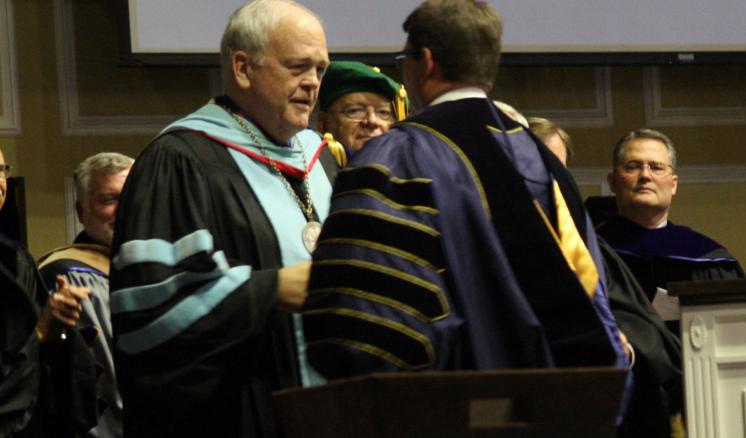 President Dr. Blackburn shaking hands with others dressed in graduation ceremony.