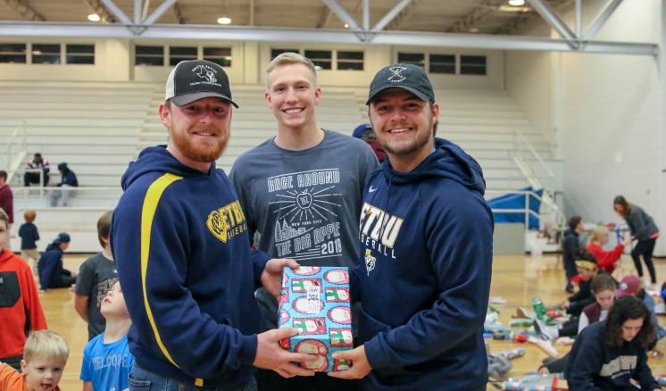 Three male student-athletes show the OCC boxes they put together