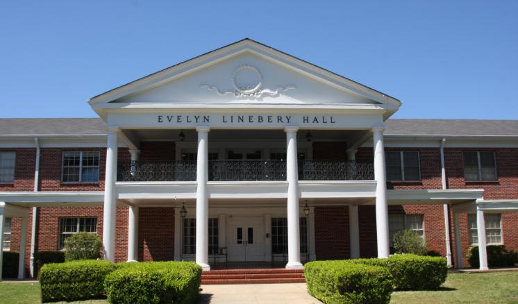 A brick residence hall building with white columns at East Texas Baptist University with a blue sky in the background.