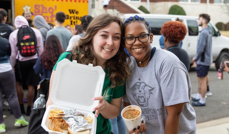 Two women smiling at the camera with food in their hands
