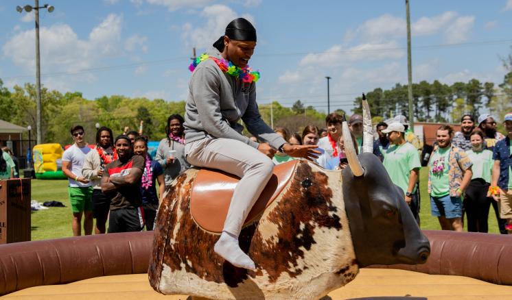 Man riding a mechanical bull with a crowd watching in the background