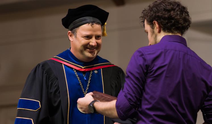 Man in graduation regalia giving a plaque to another man