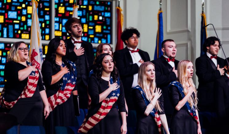 Choir students with their hands over their hearts with American Flag sashes on