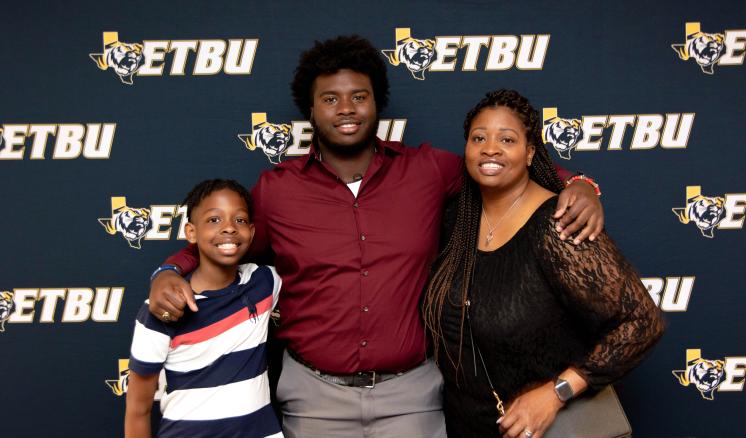 Two men and a woman smiling at the camera in front of a navy blue ETBU backdrop