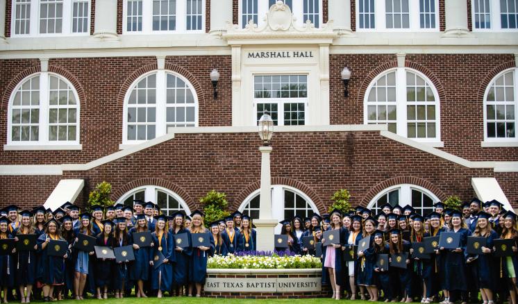 A group of students in graduation regalia in front of Marshall Hall
