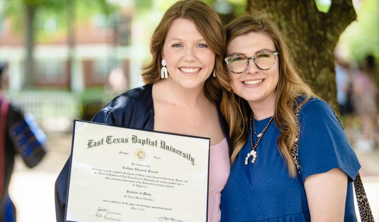 Two women smiling at the camera with one holding an ETBU diploma