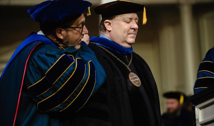 Two men in graduation regalia on a stage