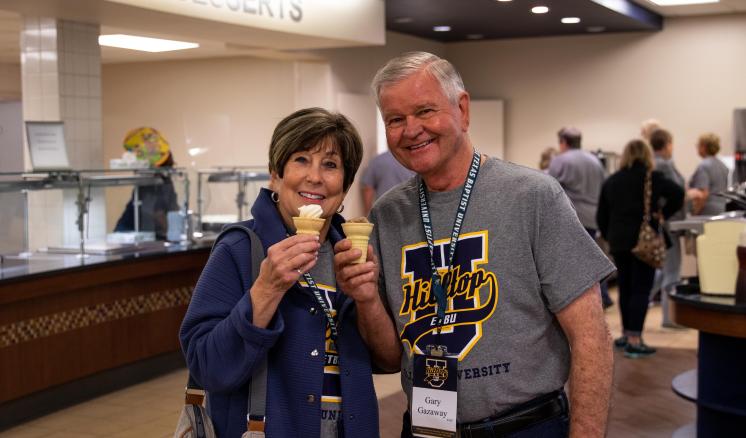 A man and a woman smiling at the camera with ice cream cones in hand