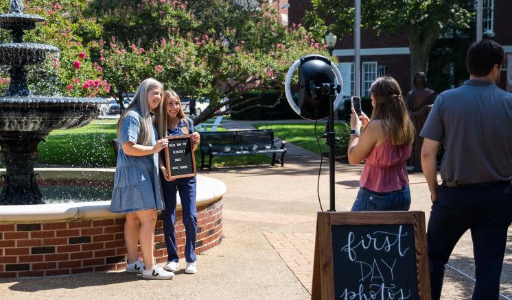 A group of students taking pictures with a sign in their hands