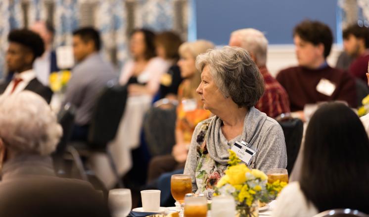 Picture of older lady looking towards the stage at a table with people in the background