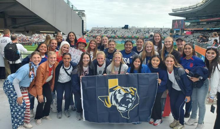 Female group outside at a soccer stadium holding a ETBU flag looking at the camera