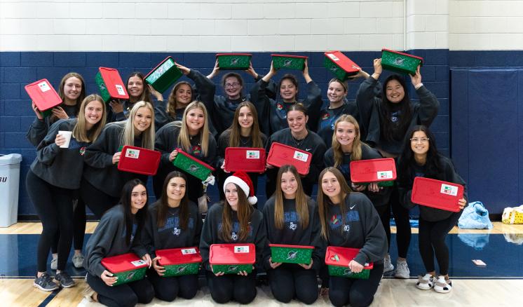 Group of female students holding Operation Christmas Child boxes smiling at the camera 