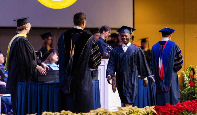 Male student walking across the stage at graduation in navy cap and gown