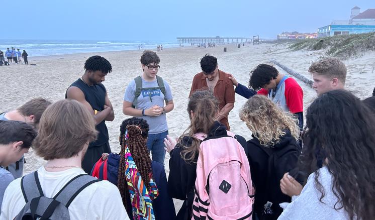 A group individuals form a prayer circle on the beach