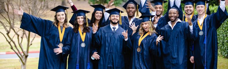 Group of graduates in their caps and gowns smiling at the camera with their hands up