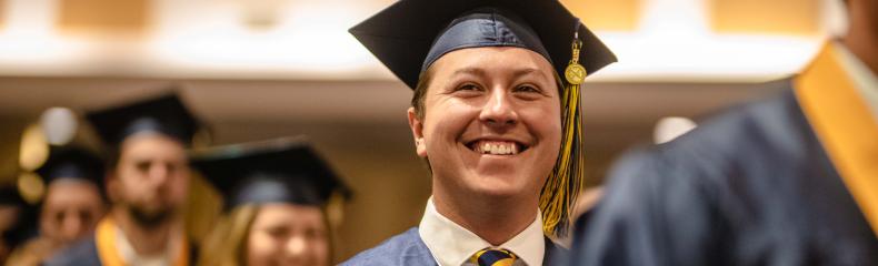 A man smiling in his graduation regalia in a line of other students
