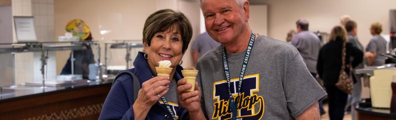 A man and a woman smiling at the camera with ice cream cones in hand