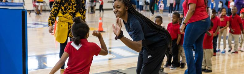 A woman giving a high five to a little boy in the gym with other people in the background