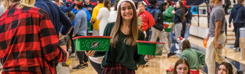 Woman smiling at camera with christmas boxes in hand with groups of people in the background