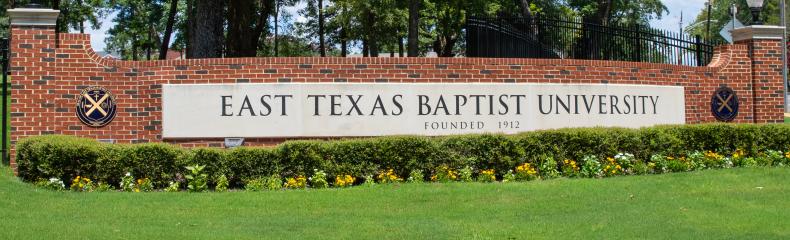 A brick wall with East Texas Baptist University logo with a blue sky in the background