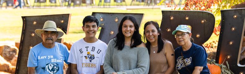 Group of males and females sitting smiling at the camera in front of a ETBU sign