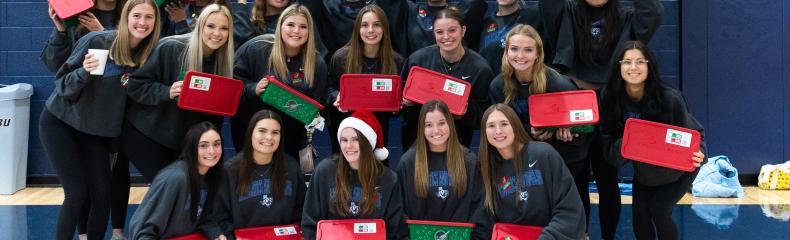 Group of female students holding Operation Christmas Child boxes smiling at the camera 