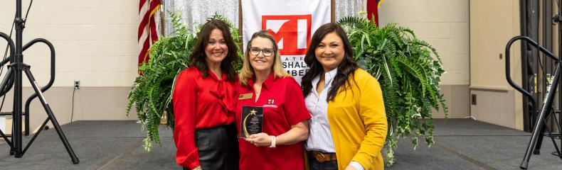 Three women posing with employee of the year award smiling at the camera 