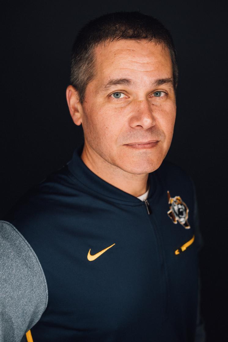 A man smiling at the camera in front of a navy backdrop.