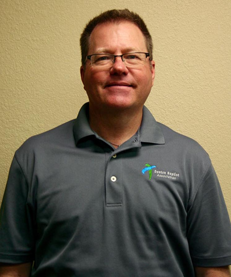 A man standing in front of a wall wearing a gray shirt