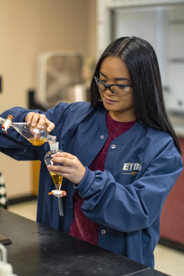 A woman pouring a liquid into a glass beaker
