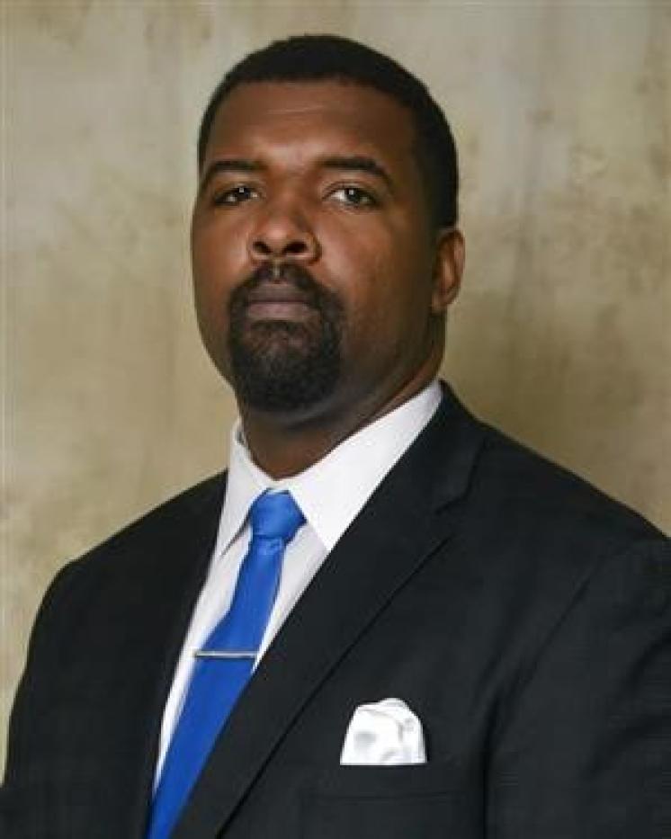 Professional headshot of an man in a suit and blue tie.