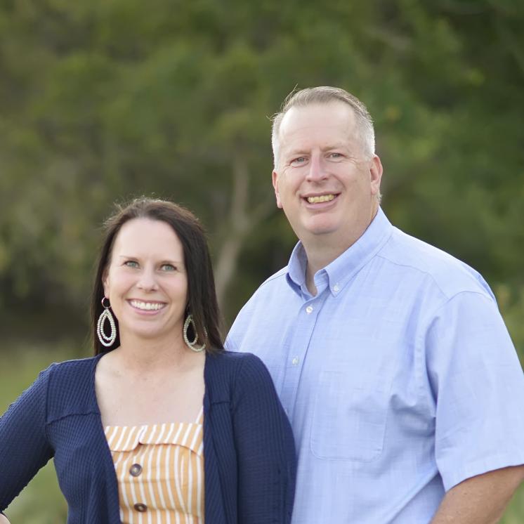 A man and a woman outside in nice clothes on grass in front of a tree background