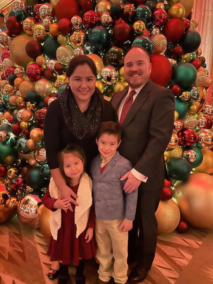 A an and a woman standing with their children behind large christmas ornaments inside