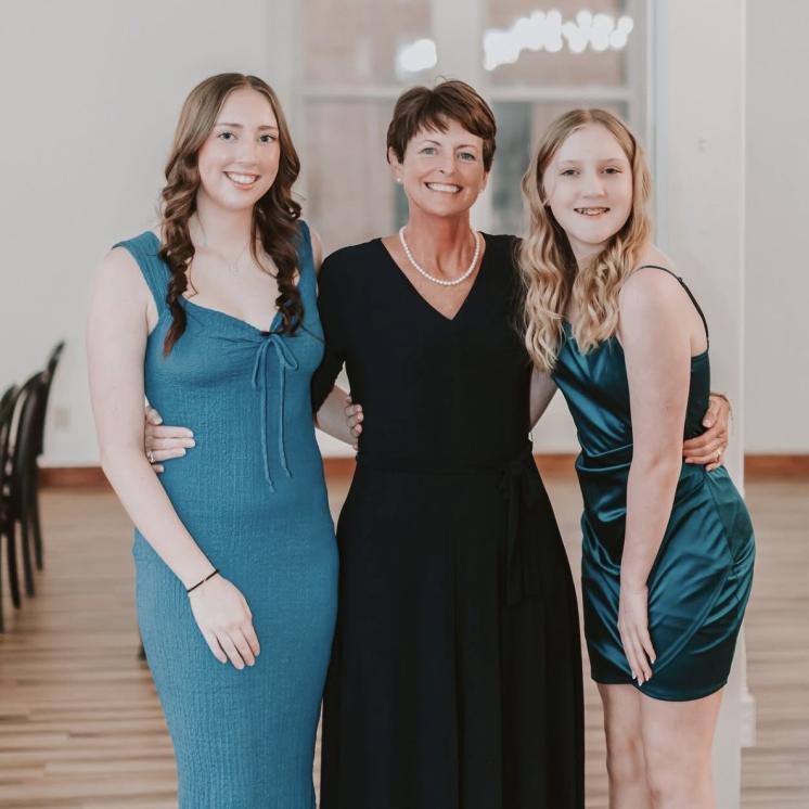 A woman standing hugging her two daughters