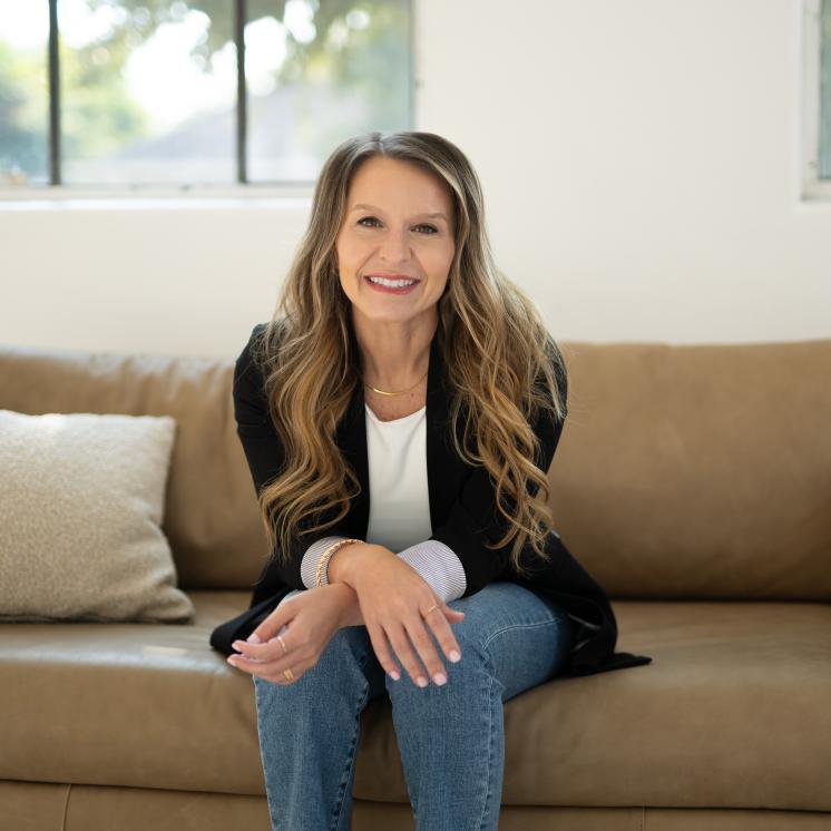 A woman in fromal clothing sat on a brightly colored couch with arms crossed