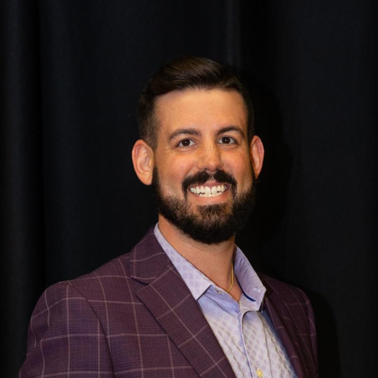 A man stood in formal attire smiling with a black backdrop