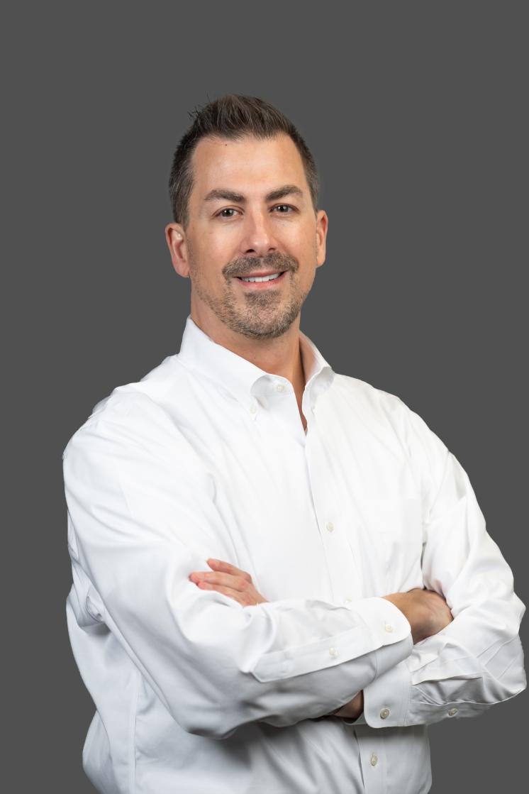 A man in a white button down shirt standing against a grey background