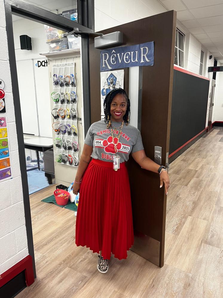 A woman standing in a doorway wearing a red skirt and a grey tshirt.