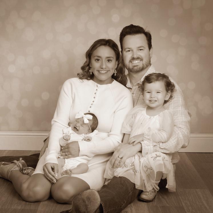 Husband, wife, toddler, and baby sitting smiling in a sepia portrait.