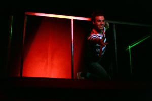 A man standing on a dark lit stage with a red light behind him