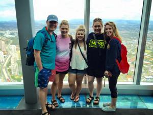 Five people standing on a glass floor in front of tall windows with a cityscape view.