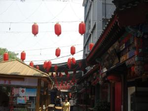 Outdoor market scene with red lanterns hanging overhead and traditional buildings.