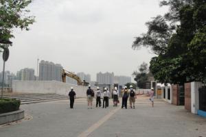 A group of people in safety gear walks toward a construction site with high-rise buildings in the background.
