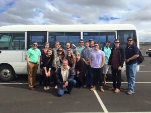 A group of people smiling and sitanding outside of a white bus
