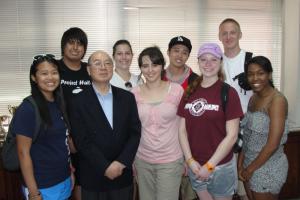 A group of nine people smiling indoors, with one man in a suit and others in casual attire.