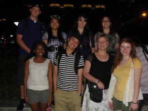 Group of eight people smiling outdoors at night.